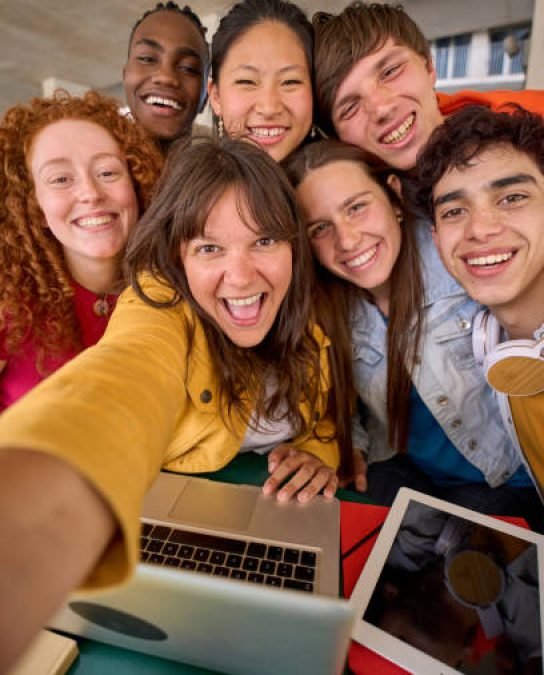 frds Vertical selfie with mobile phone of multiracial cheerful group of students gathered in hall of university building. Happy young friends hugging laughing and posing for photo. People smiling on campus